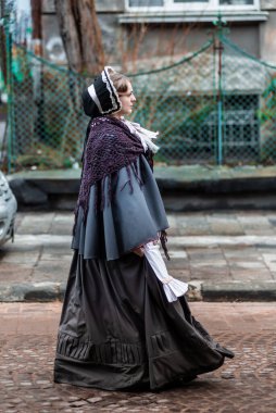 Ondokuzuncu yüzyıl kadını, zarif giyimli, bir kalenin avlusunda yürüyor.