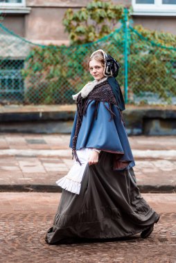 Ondokuzuncu yüzyıl kadını, zarif giyimli, bir kalenin avlusunda yürüyor.