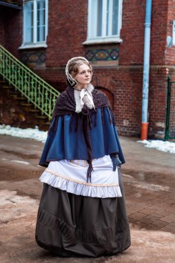 Ondokuzuncu yüzyıl kadını, zarif giyimli, bir kalenin avlusunda yürüyor.