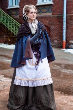 Ondokuzuncu yüzyıl kadını, zarif giyimli, bir kalenin avlusunda yürüyor.