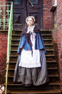 Ondokuzuncu yüzyıl kadını, zarif giyimli, bir kalenin avlusunda yürüyor.