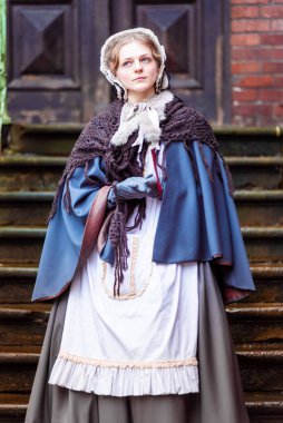 Ondokuzuncu yüzyıl kadını, zarif giyimli, bir kalenin avlusunda yürüyor.