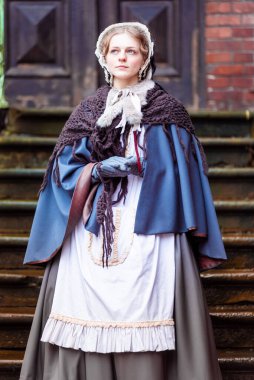 Ondokuzuncu yüzyıl kadını, zarif giyimli, bir kalenin avlusunda yürüyor.