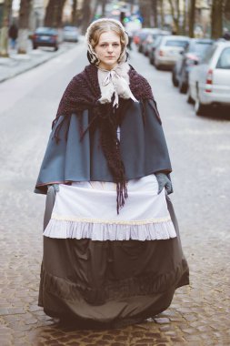 Ondokuzuncu yüzyıl kadını, zarif giyimli, bir kalenin avlusunda yürüyor.