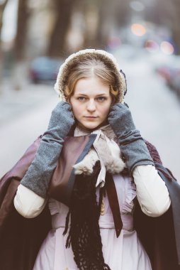 Ondokuzuncu yüzyıl kadını, zarif giyimli, bir kalenin avlusunda yürüyor.