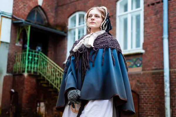 Nineteenth-century woman, elegantly dressed, walks through the courtyard of a castle