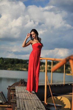 Tropikal bir plajda koşan uzun kırmızı elbiseli güzel bir genç kadın. Arka planda mavi deniz.