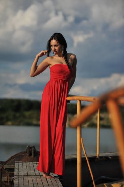 Tropikal bir plajda koşan uzun kırmızı elbiseli güzel bir genç kadın. Arka planda mavi deniz.