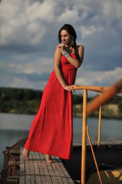 Tropikal bir plajda koşan uzun kırmızı elbiseli güzel bir genç kadın. Arka planda mavi deniz.