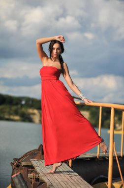Güzel bir kadının kumda kırmızı elbiseyle serinlerken çekilmiş moda fotoğrafı.