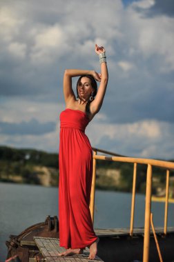 Tropikal bir plajda koşan uzun kırmızı elbiseli güzel bir genç kadın. Arka planda mavi deniz.