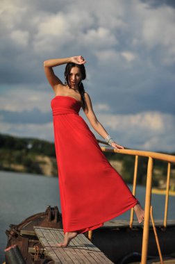Güzel bir kadının kumda kırmızı elbiseyle serinlerken çekilmiş moda fotoğrafı.