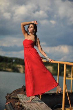 Tropikal bir plajda koşan uzun kırmızı elbiseli güzel bir genç kadın. Arka planda mavi deniz.