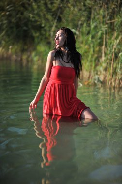 Tropikal bir plajda koşan uzun kırmızı elbiseli güzel bir genç kadın. Arka planda mavi deniz.