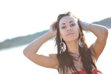 Tropikal bir plajda koşan uzun kırmızı elbiseli güzel bir genç kadın. Arka planda mavi deniz.