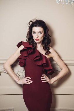 Güzel, seksi, genç, esmer, uzun dalgalı saçlı, ince vücutlu, harika vücutlu, güzel makyajlı, zayıf elbiseli bir kadın.