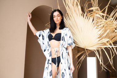 Siyah mayolu güzel bir kadın büyük bir duvarın arkasında poz veriyor.