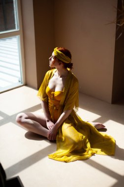 Sarı elbiseli güzel bir kadın iç mekanda poz veriyor.