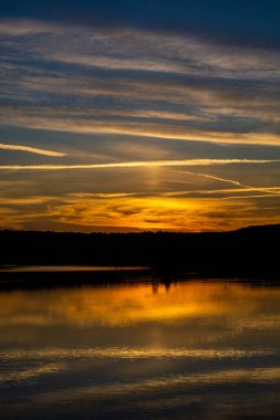 Gölün kıyısında gün batımı. Doğa manzarası. Yansıma, mavi gökyüzü ve sarı güneş ışığı. Gün batımında manzara.