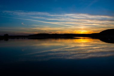 Gölün kıyısında gün batımı. Doğa manzarası. Yansıma, mavi gökyüzü ve sarı güneş ışığı. Gün batımında manzara.