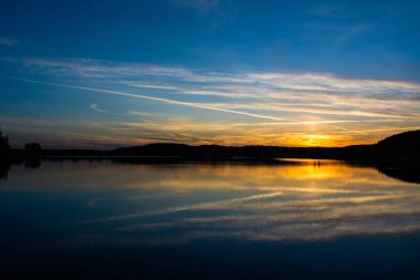 Gölün kıyısında gün batımı. Doğa manzarası. Yansıma, mavi gökyüzü ve sarı güneş ışığı. Gün batımında manzara.