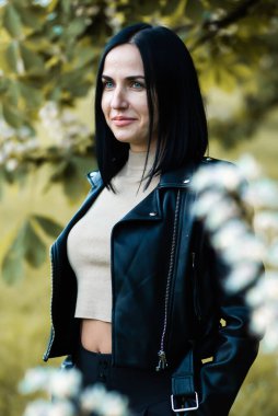 Siyah elbiseli ve parkın arka planında ceketli güzel bir genç kadının portresi.