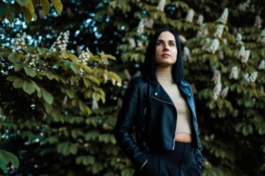 Siyah ceketli ve güneş gözlüklü güzel bir kadın sokakta poz veriyor.