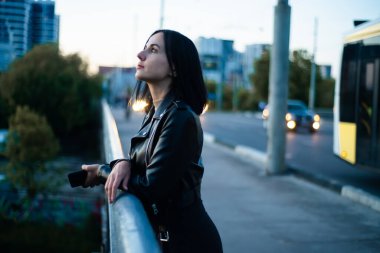 Siyah takım elbiseli, güneş gözlüklü genç ve güzel bir kadın sokakta poz veriyor.