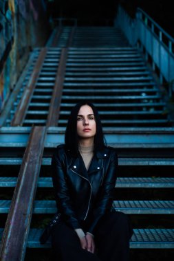 Siyah ceketli ve mavi gömlekli genç bir kadın ve şehrin arka planında bir eşarp.