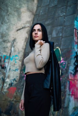 Siyah ceketli, mavi gömlekli, beyaz bluzlu, tuğladan bir arka planda güzel bir kız.