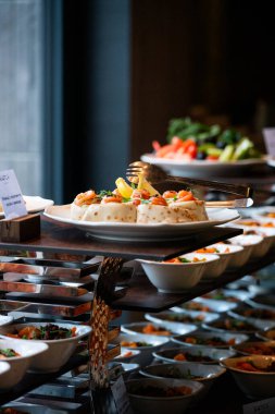 Profesyonel bir yemek servisinde salata, aperatif ve sıcak yemeklerin yer aldığı açık büfe masasında çeşitli taze yemekler sergileniyor.