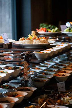 Profesyonel bir yemek servisinde salata, aperatif ve sıcak yemeklerin yer aldığı açık büfe masasında çeşitli taze yemekler sergileniyor.