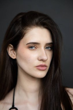 Gri arka planda doğal makyajı olan genç bir esmerin portresi..
