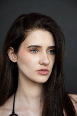 Siyah makyajlı, genç ve güzel bir kız. Stüdyoda gri arka planda poz veriyor.