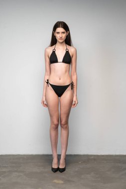 Siyah iç çamaşırlı, beyaz arka plan duvarında poz veren genç ve güzel seksi bir kız.