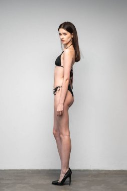 Uzun boylu, siyah iç çamaşırlı güzel bir kadın duvarın önünde duruyor.