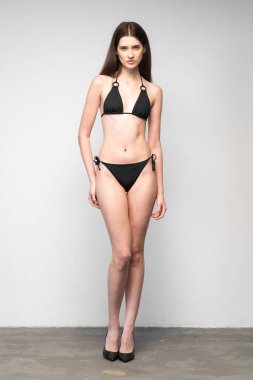 Siyah iç çamaşırlı güzel bir kadın beyaz bir arka planın önünde poz veriyor.