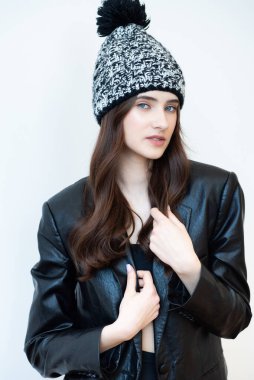 Siyah ceketli, siyah şapkalı, beyaz arka planda kapüşonlu güzel bir kadın.
