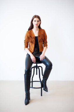 Deri ceketli ve kot pantolonlu güzel bir kadın sandalyede oturuyor..