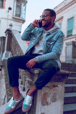 Siyah çocuk merdivende cep telefonu kullanarak oturuyor.