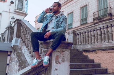 Siyah çocuk merdivende cep telefonu kullanarak oturuyor.