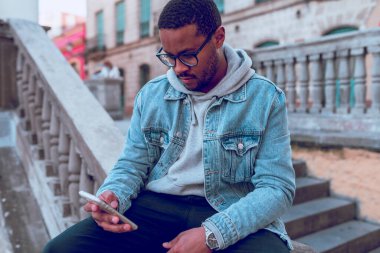 Siyah çocuk merdivende cep telefonu kullanarak oturuyor.