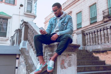 Siyah çocuk merdivende cep telefonu kullanarak oturuyor.