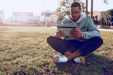 Siyah çocuk parkta tablet kullanarak oturuyor.