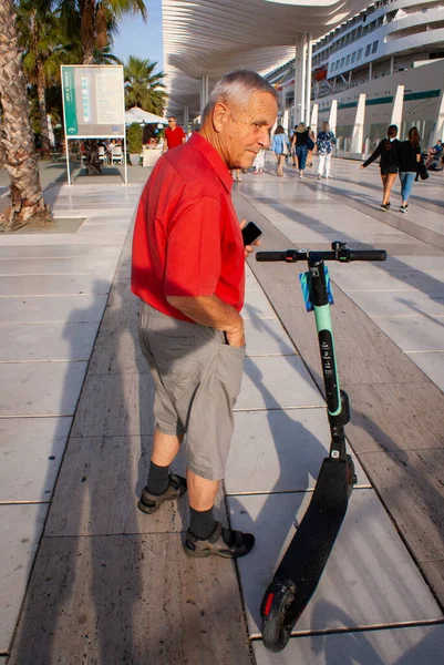 18\ 10\ 19. Malaga, İspanya. Akıllı telefonu elinde, elektrikli scooter 'ın yanındaki yaşlı adam.