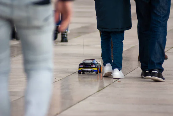 Electric toy car or hot wheel on the sidewalk. Shoes and legs of a child