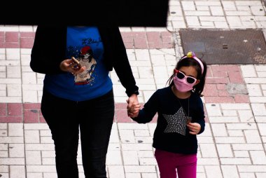 26.04.20. Malaga, İspanya. Kaldırımda annesinin yanında pembe yüz maskesi ve güneş gözlüğü takan genç bir kız elini tutuyor.