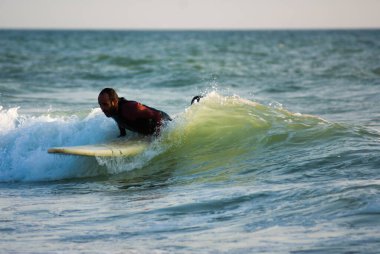 Cadiz, İspanya. Eylül 2020. Sörf tahtasında yatan ve dalgıç kıyafeti giymiş bir dalgayı yakalayan adam.