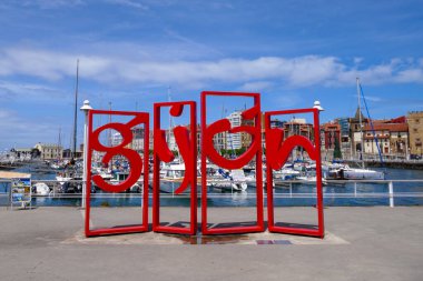 Letronas rojas Gijon. Büyük kırmızı harfli mesaj. Heykel, limanda heykel. Asturias, İspanya. Femetal