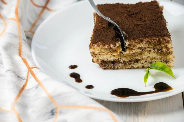 Çikolata şurubu ve ahşap arka planda beyaz tabakta tatlı Tiramisu.